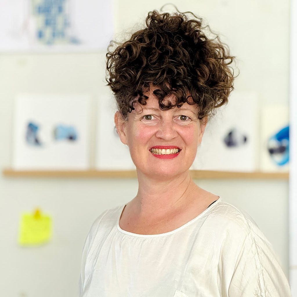 Kiharatukkainen hymyilevä nainen, taustalla näkyy taidetta.