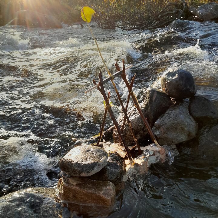 Close-up of the rapids, in the foreground a work of art built from branches on top of rocks, a small watermill.