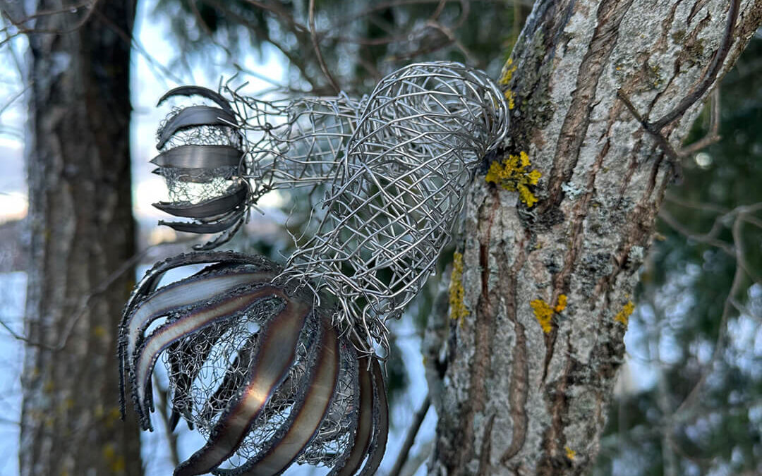 Puuhun on kiinnitetty metallipalasista ja metallilangasta punottu taideteos.