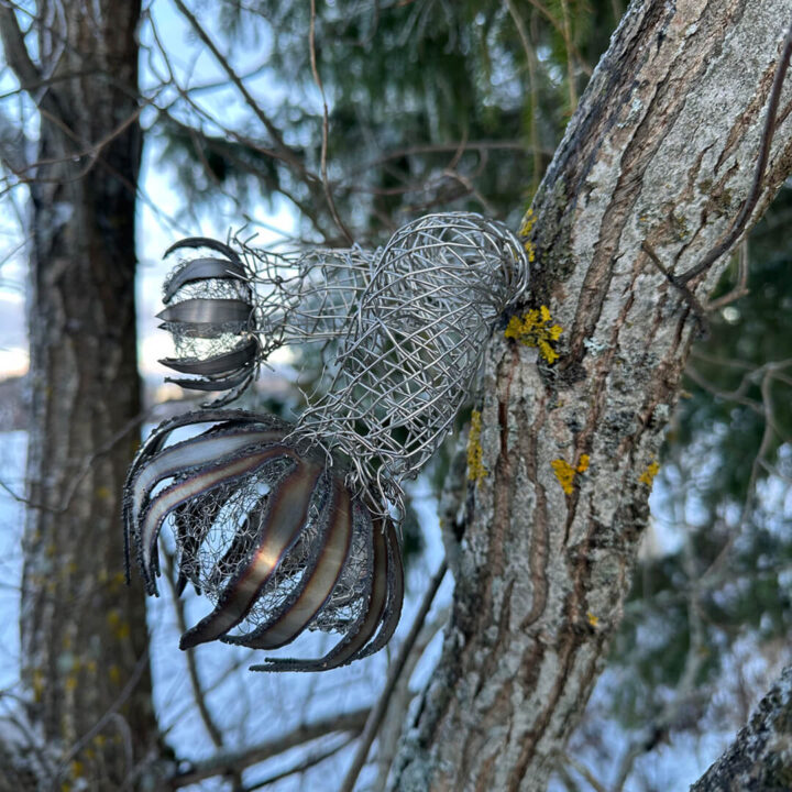 An artwork woven from metal pieces and metal wire attached to a tree.