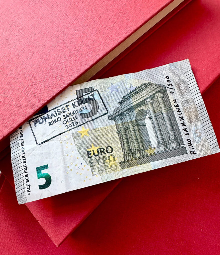 A five-euro bill with the stamp in Finnish "Red books, Riiko Sakkinen, Oulu 2026" placed on red books.
